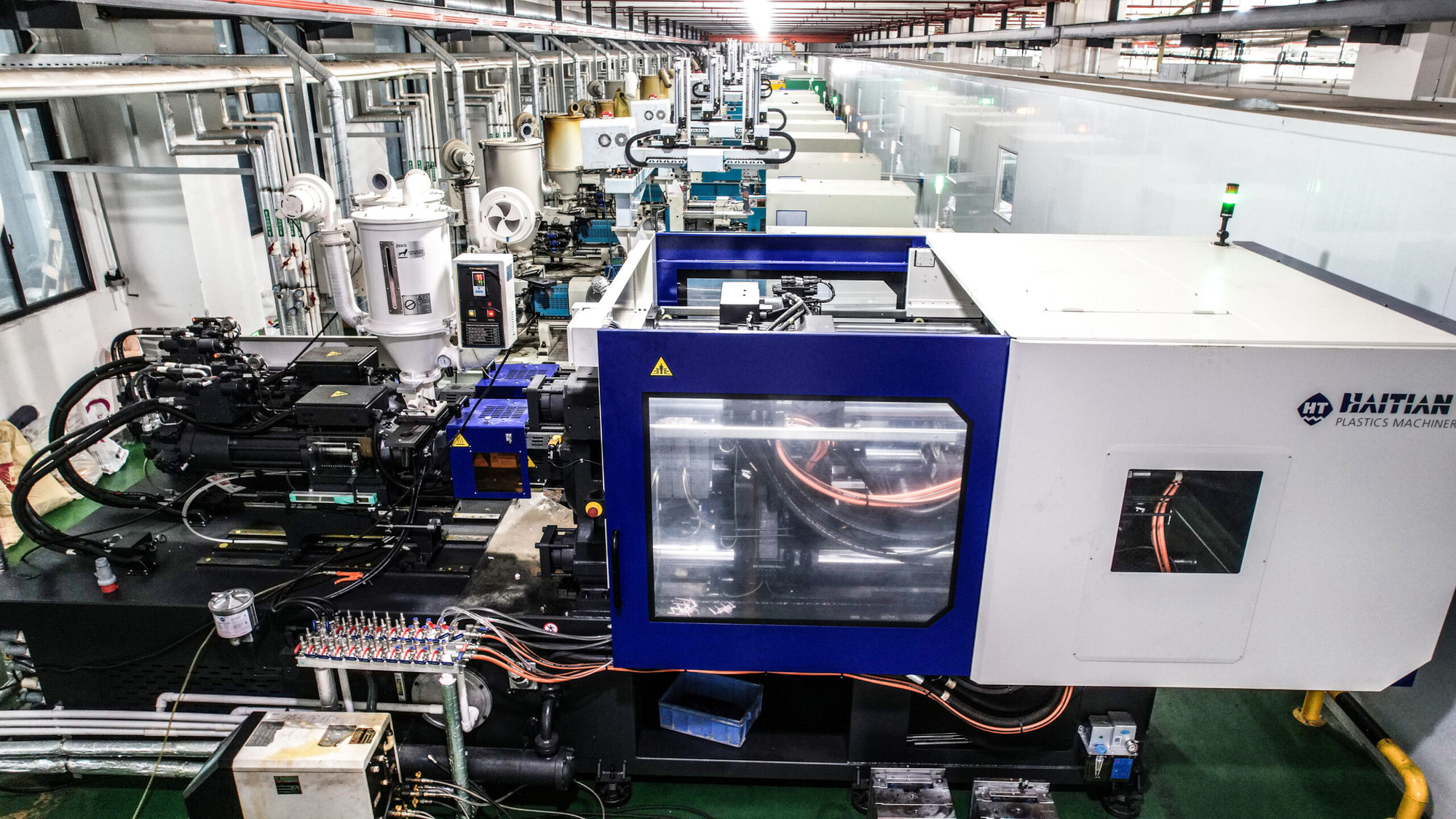 High-quality photo of modern manufacturing facility with plastic injection molding machines silicone molds and CNC prototypes on tables, Hong Kong and Vietnam factory elements, clean professional lighting, realistic style, blue industrial tones, focus on precision parts, no text, horizontal composition